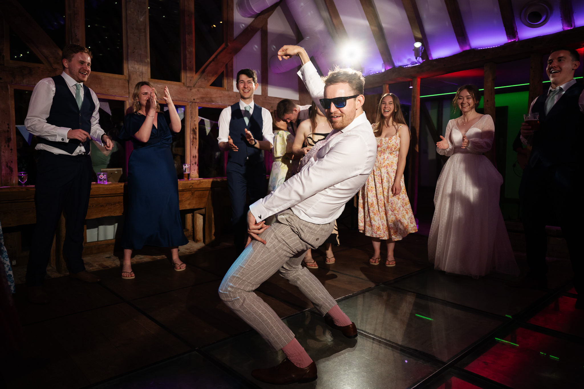 Wedding guest wearing sunglasses dancing as friends cheer at South Farm