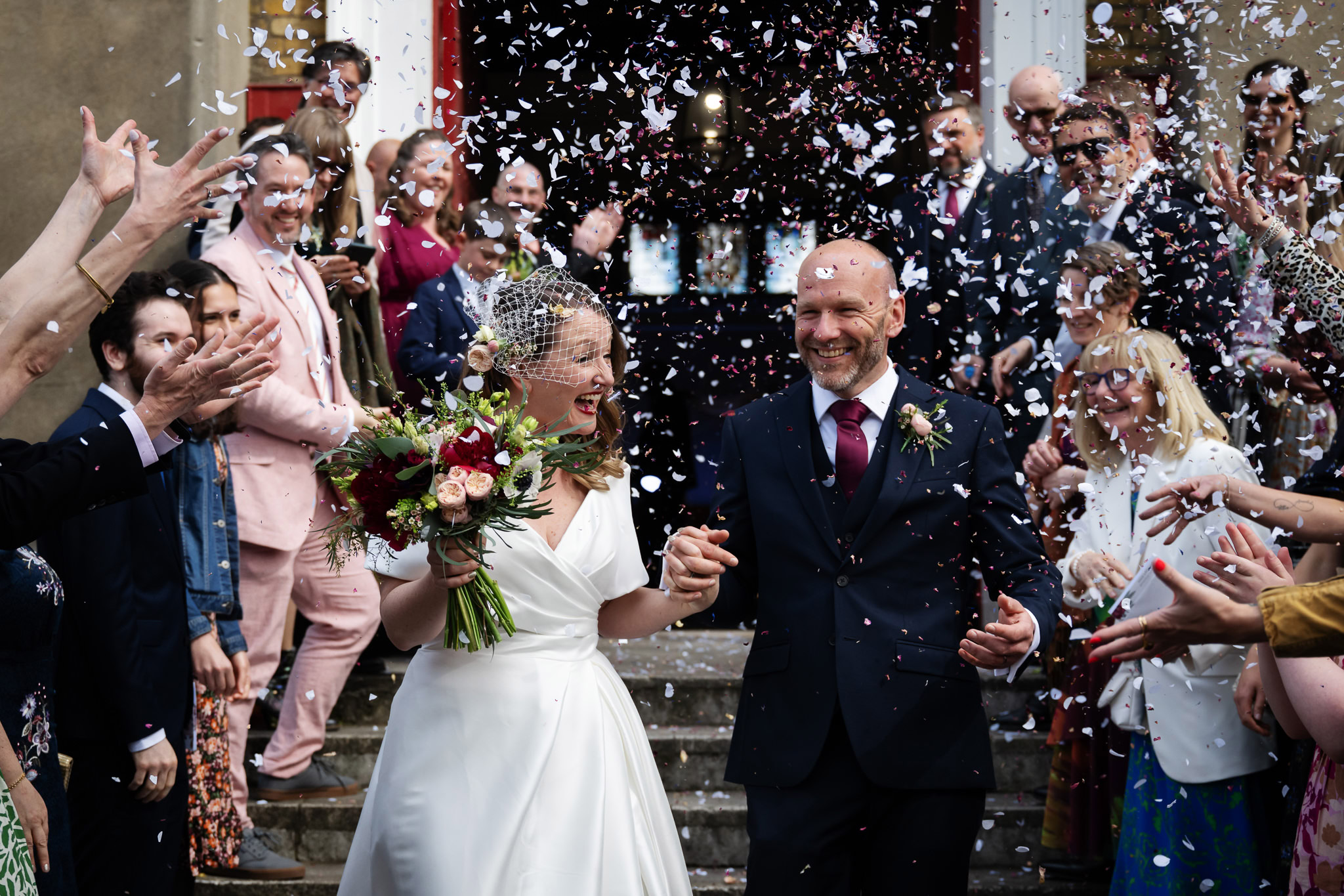 Bride and groom laughing as wedding guests shower them with confetti outside their London wedding ceremony